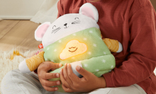 A child holds the Fisher-Price toy Meditation Mouse in their lap. 