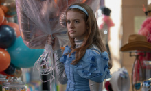 A young woman dressed up as Cinderella looks grumpy holding helium balloons.