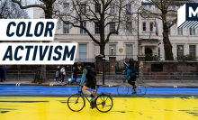 A cyclist passes over a giant Ukrainian flag painted over the Russian Embassy in London. Caption reads: Colored Activism