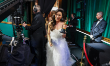 Michelle Yeoh holds her Oscar trophy while walking past crew members behind the stage at the Academy Awards. 