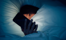 Woman hiding under the blanketed and using smart phone at late night on bed