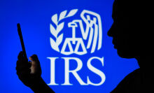 Silhouette of person holding phone over blue IRS background