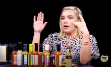 A woman sits at a table in front of a row of hot sauces.