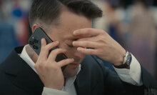 A man on the phone puts a hand to his face and closes his eyes.