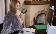 woman sitting at computer with blanket and drinking coffee