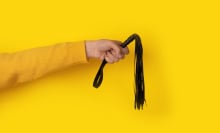 Leather whip in hand over yellow background