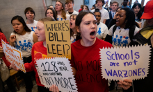 A group of young people in red and white shirts march and chant through a legislative building. They hold signs reading, "Schools are not warzones", "Ban assault weapons", "Where's Bill Lee?", and "128  mass shooting this year. No more."