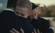 Two men and a woman group hug while crying. 