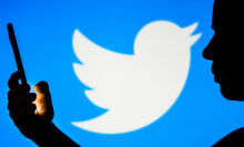 In this photo illustration, a woman's silhouette holds a smartphone with the Twitter logo in the background.