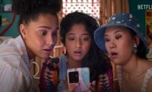 Devi (Maitreyi Ramakrishnan) and her two friends look over a phone in a still.