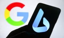 A silhouetted hand holds a phone with the blue Bing logo on the screen. Behind the phone is a Google logo in the background.