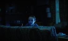 A young girl looks over a couch in a blue-lit living room. 