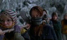 A group of teenage girls carry a body tied to a wooden pole through the snowy wilderness.