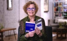 Judy Blume, wearing blue-rimmed glasses and a green blouse, reads from her book "Are You There God? It's Me, Margaret."