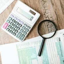 Tax forms next to a calculator and a magnifying glass
