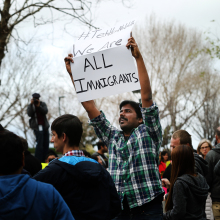 A man holds up a sign in the middle of a protest crowd. The sign reads "We are all Immigrants."