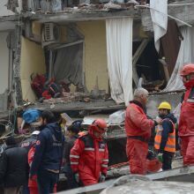 A group of emergency relief workers in red jumpsuits walk through the rubble of a building. 