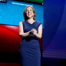 Susan Wojcicki from the knees up, smiling in a navy blue shift dress,