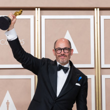 Director Edward Berger, wearing black and white formal wear accented with a blue ribbon, holds his Oscar at the 95th Academy Awards