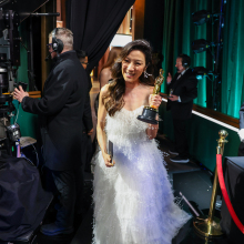 Michelle Yeoh holds her Oscar trophy while walking past crew members behind the stage at the Academy Awards. 