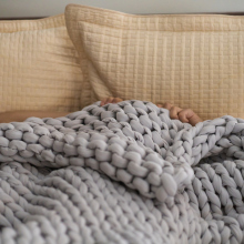 A woman lies under a knitted blanket in bed with just her hands visible. 