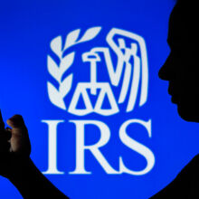 Silhouette of person holding phone over blue IRS background