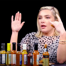A woman sits at a table in front of a row of hot sauces.