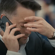 A man on the phone puts a hand to his face and closes his eyes.