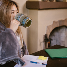 woman sitting at computer with blanket and drinking coffee