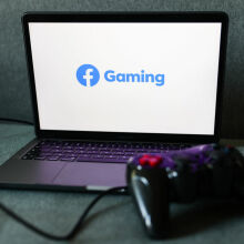 Facebook Gaming logo displayed on a laptop screen, with a gamepad resting in front of it.