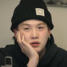 Suga from BTS wears a beanie and holds his hand under his chin.