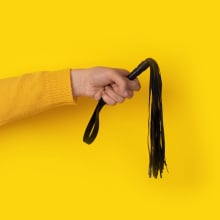 Leather whip in hand over yellow background
