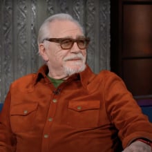 Actor Brian Cox appears on The Late Show wearing dark glasses and a bright red/orange shirt