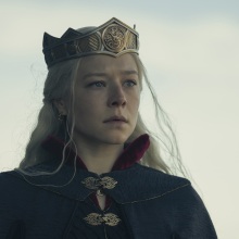 Rhaenyra Targaryen, a woman with silver blonde hair, a black cape, and a crown on her head.