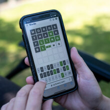 A close-up of a person playing Wordle on a smartphone outside.