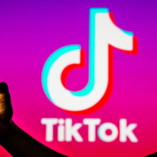 In this photo illustration, a person's silhouette holds a smartphone with the TikTok logo in the background. 