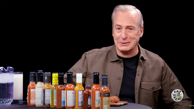 A man sits at a table in front of a row of sauce bottles.