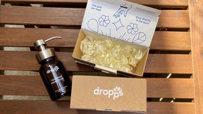 Dropps laundry detergent pod boxes and a hand soap bottle on a wood table