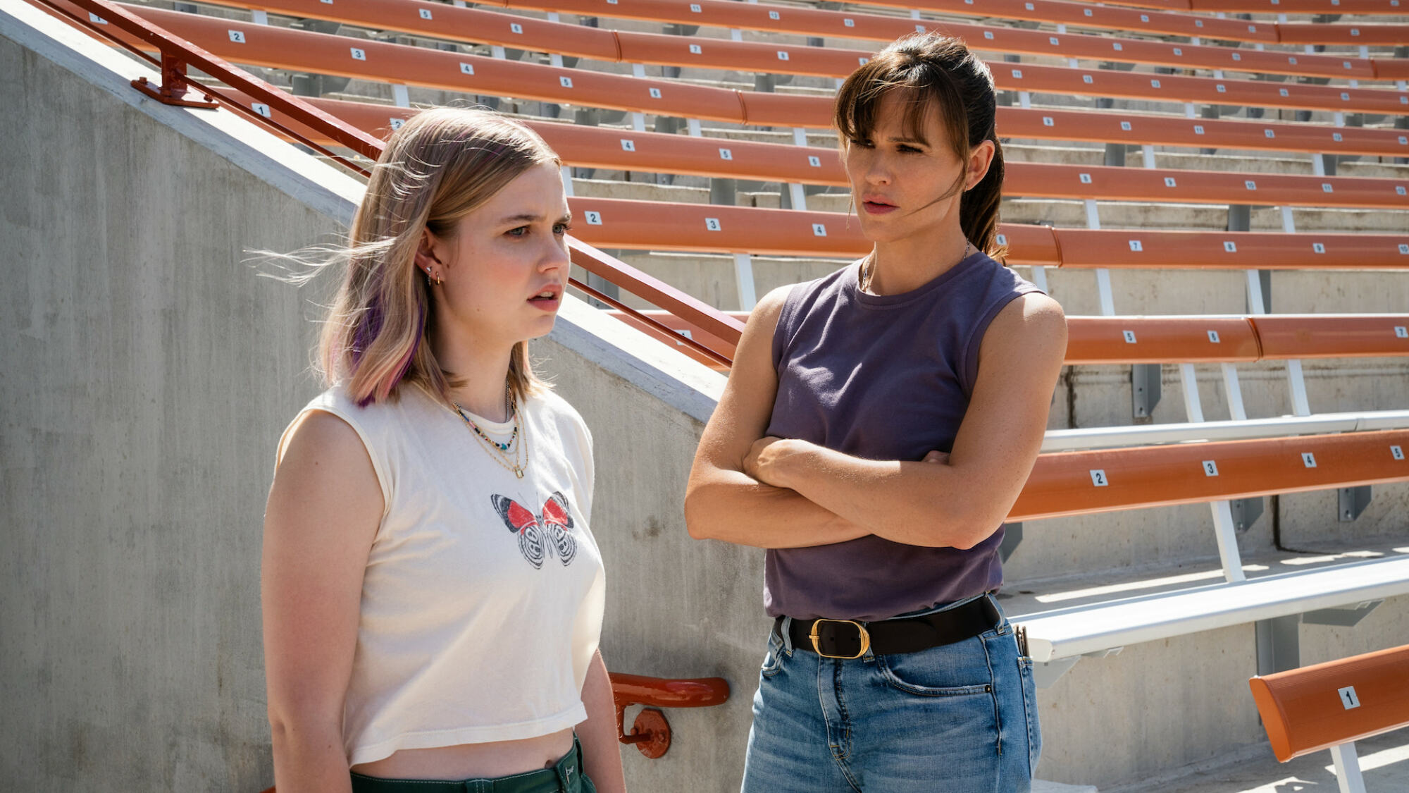 A teen and a woman stand in a school sports stadium. 