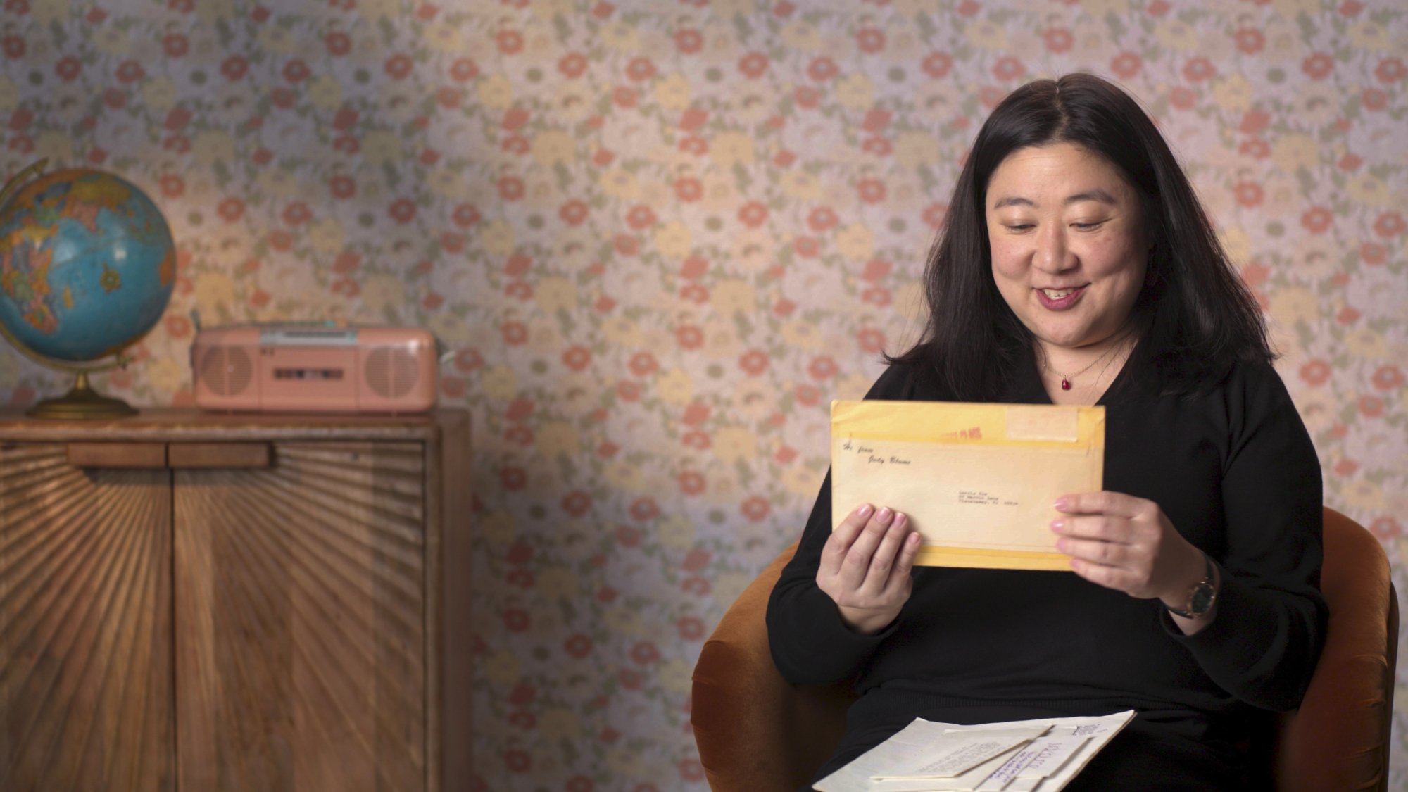 Lorrie Kim, a woman in a black blouse, holds up an envelope.