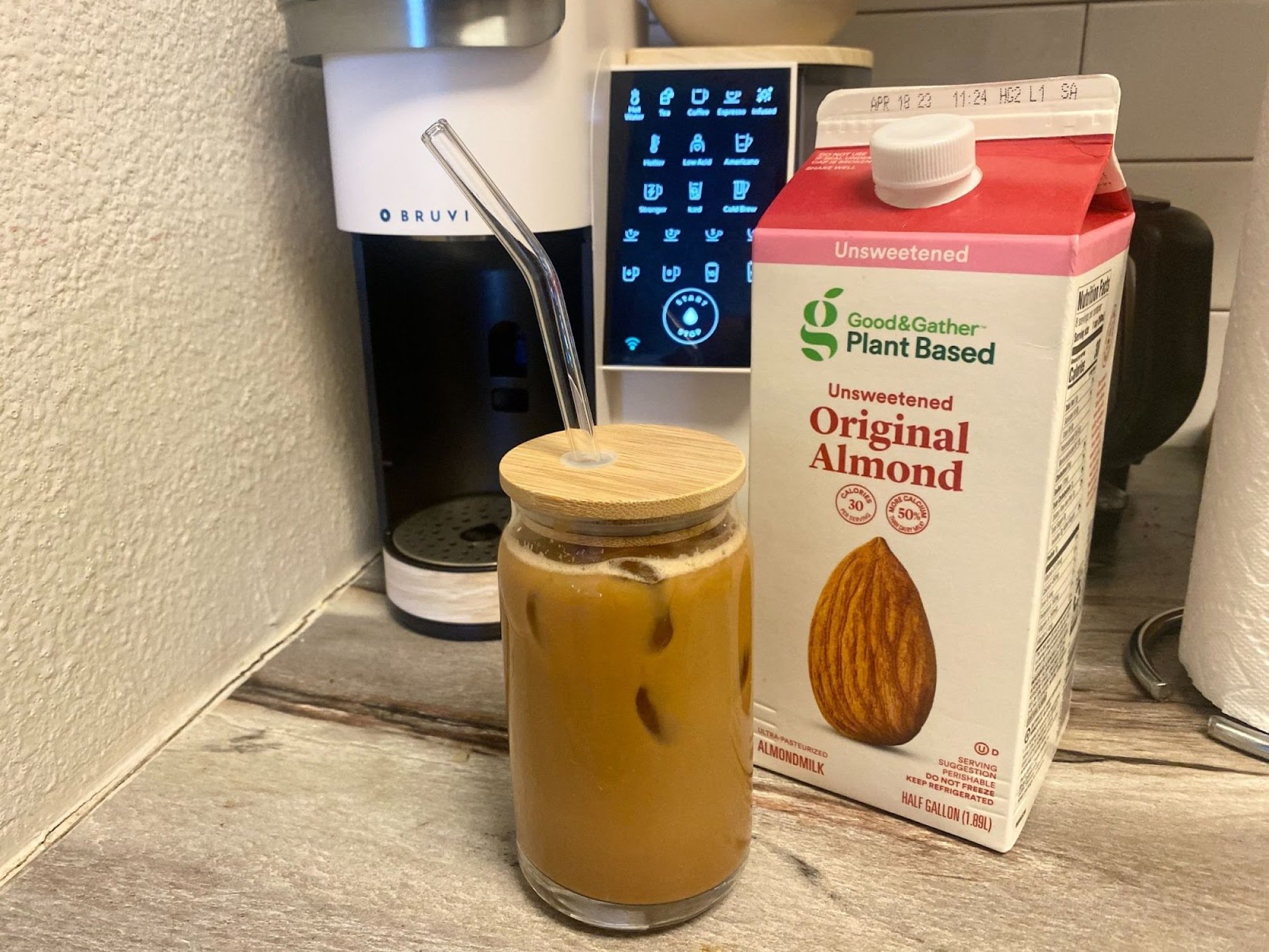 iced coffee in glass cup with straw next to carton of almond milk and Bruvi coffee maker