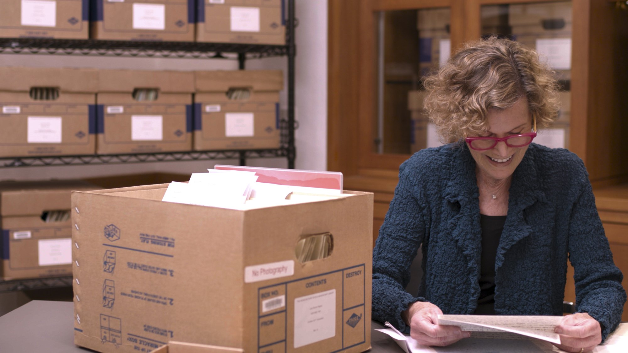Judy Blume sits in an archive, looking through a cardboard box of her letters.
