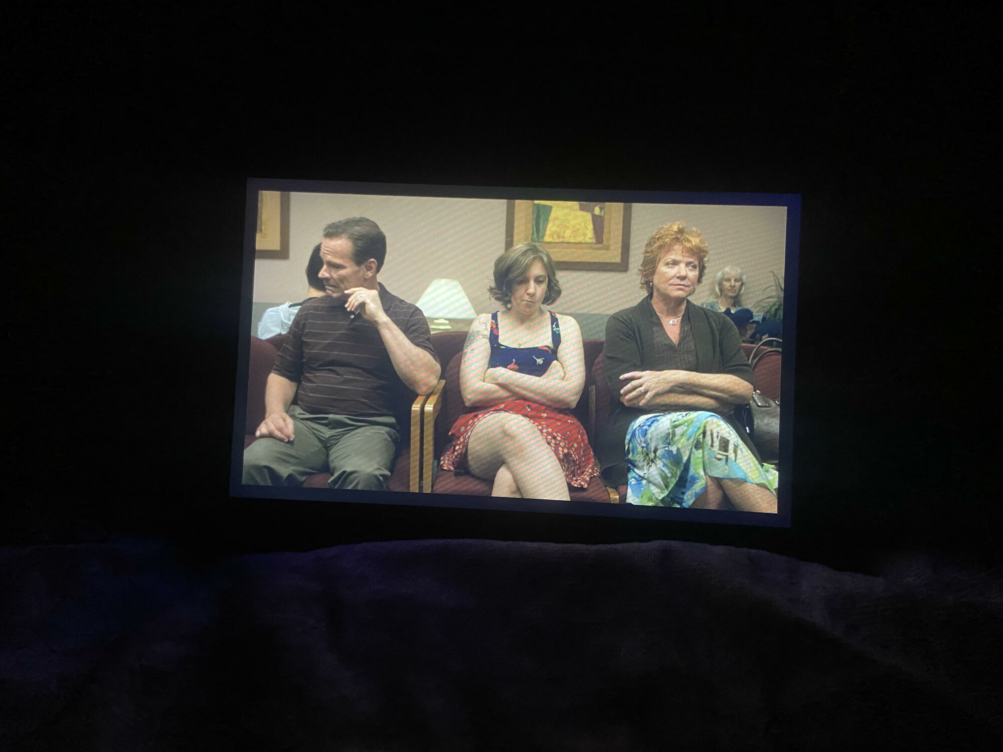 a close-up of an amazon fire 7 tablet playing an episode of "girls" on a bed in a dark room