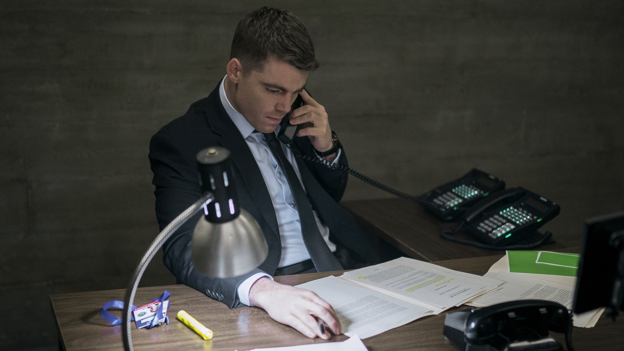 An FBI agent sits at a desk at night doing paperwork.