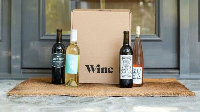 Four wine bottles next to cardboard box on doorstep