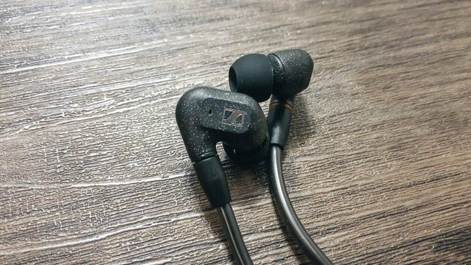 a pair of sennheiser ie 300 earbuds in black laying on a wooden table