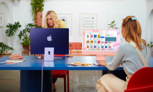 two women working on apple imacs at a blue table in a modern living room