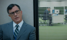 Stephen Colbert in The Late Show's Severance parody, sitting in front of an internal window like the talking-head sequences from NBC's The Office.