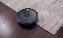 Black eufy robot vacuum against wooden floor and beige carpet