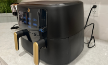 black air fryer with two gold handles and lit-up LED touch panel